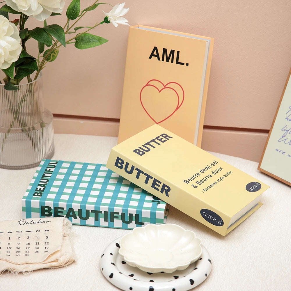 Books titled 'AML.' and 'Butter' on a surface with decorative items including a vase of flowers and a calendar.