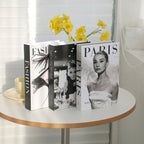 Three books on a table with a cup and yellow flowers in the background