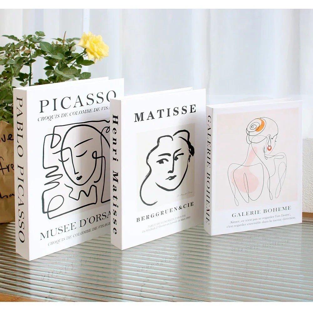 Three art-themed books on a surface with a plant in the background