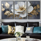 Three-panel wall art of white flowers with gold accents above a black sofa with colorful pillows.