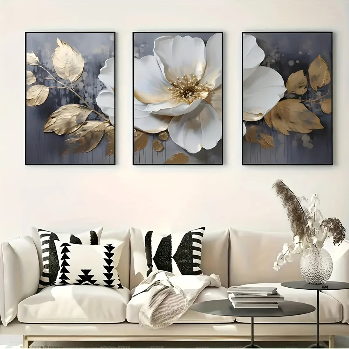 Three floral art pieces above a sofa with decorative pillows and a small table.