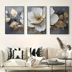 Three floral art pieces above a sofa with decorative pillows and a coffee table.