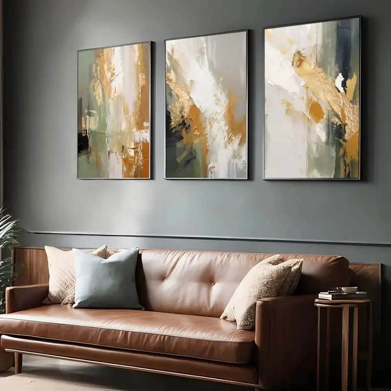 Three abstract paintings above a brown leather sofa with decorative pillows.