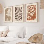 Three framed botanical prints on a wall above a sofa with decorative pillows.