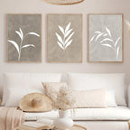 Three framed leaf prints on a wall above a sofa with decorative pillows and a hat.