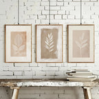 Three framed leaf prints on a white brick wall with a wooden table below.