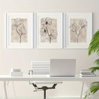 Three framed floral line art prints above a desk with a laptop and office chair.