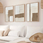 Three abstract art pieces on a wall above a white sofa with decorative pillows.