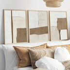 Three abstract artworks in wooden frames on a wall above a sofa with pillows.