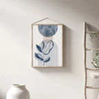 Framed abstract art print on a wall with a ladder and vase in the background