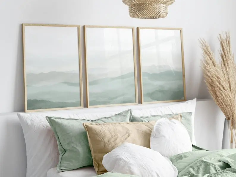 Three framed artworks on a wall above a sofa with decorative pillows.