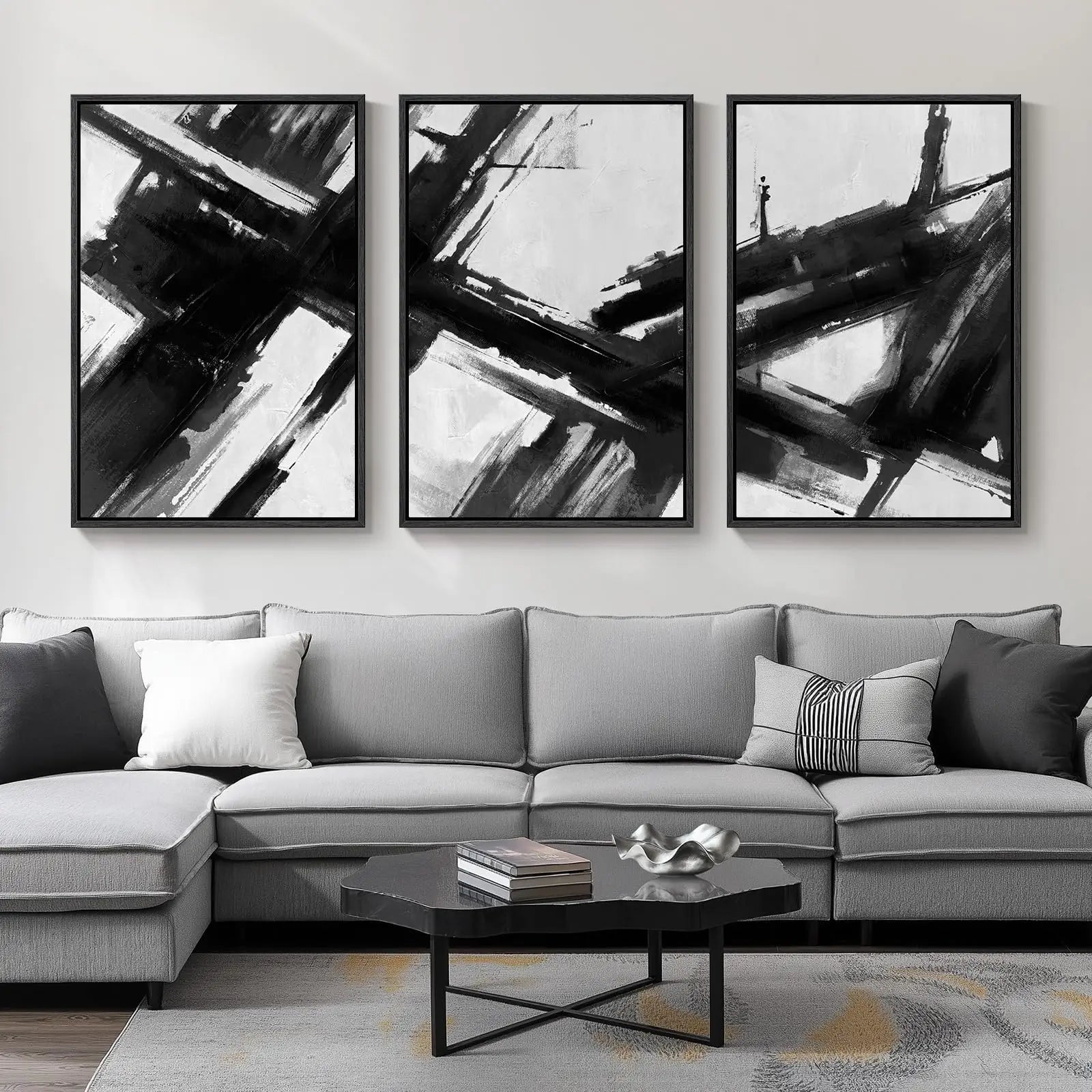 Three abstract black and white paintings above a gray sectional sofa in a living room.