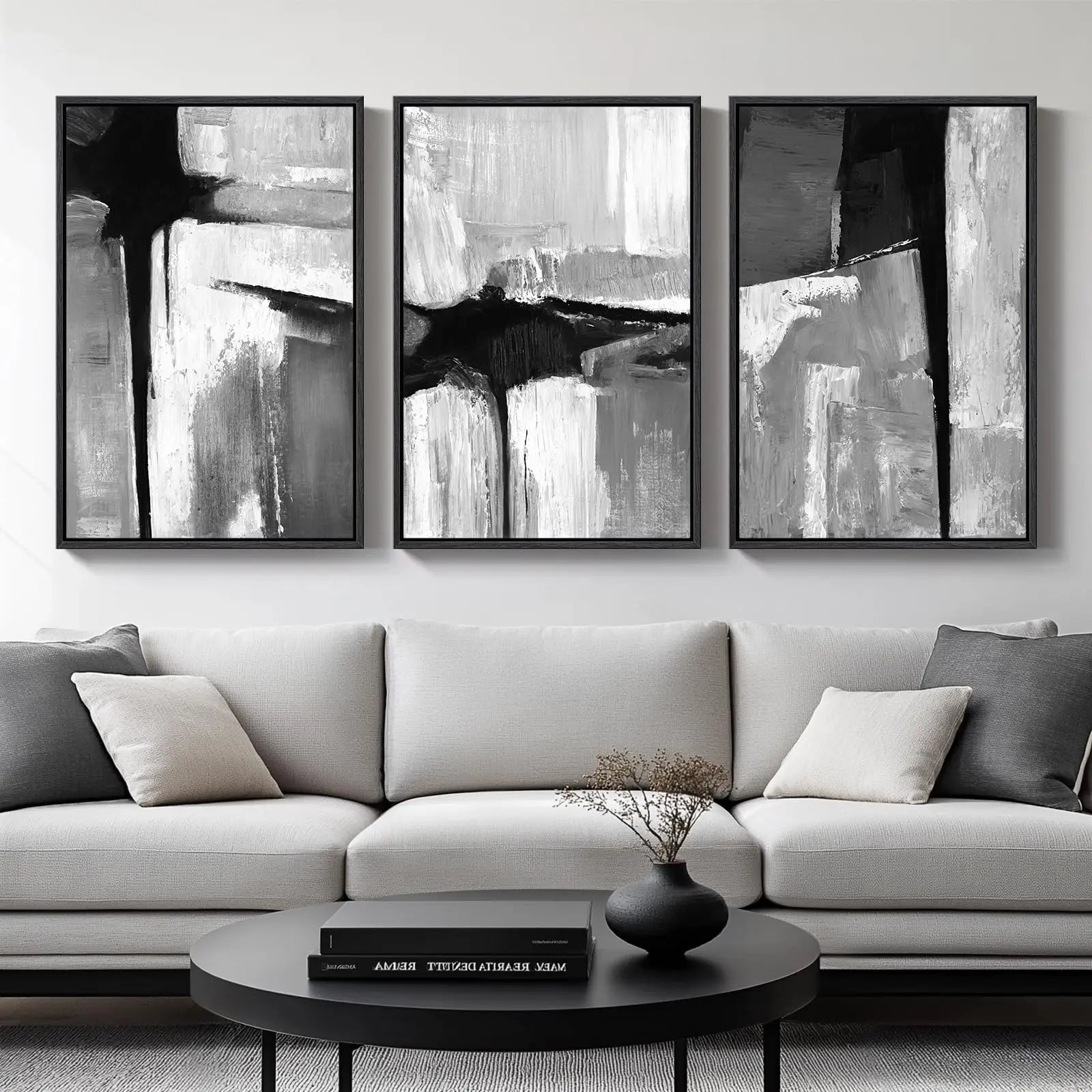 Three abstract black and white paintings above a gray sofa in a living room.