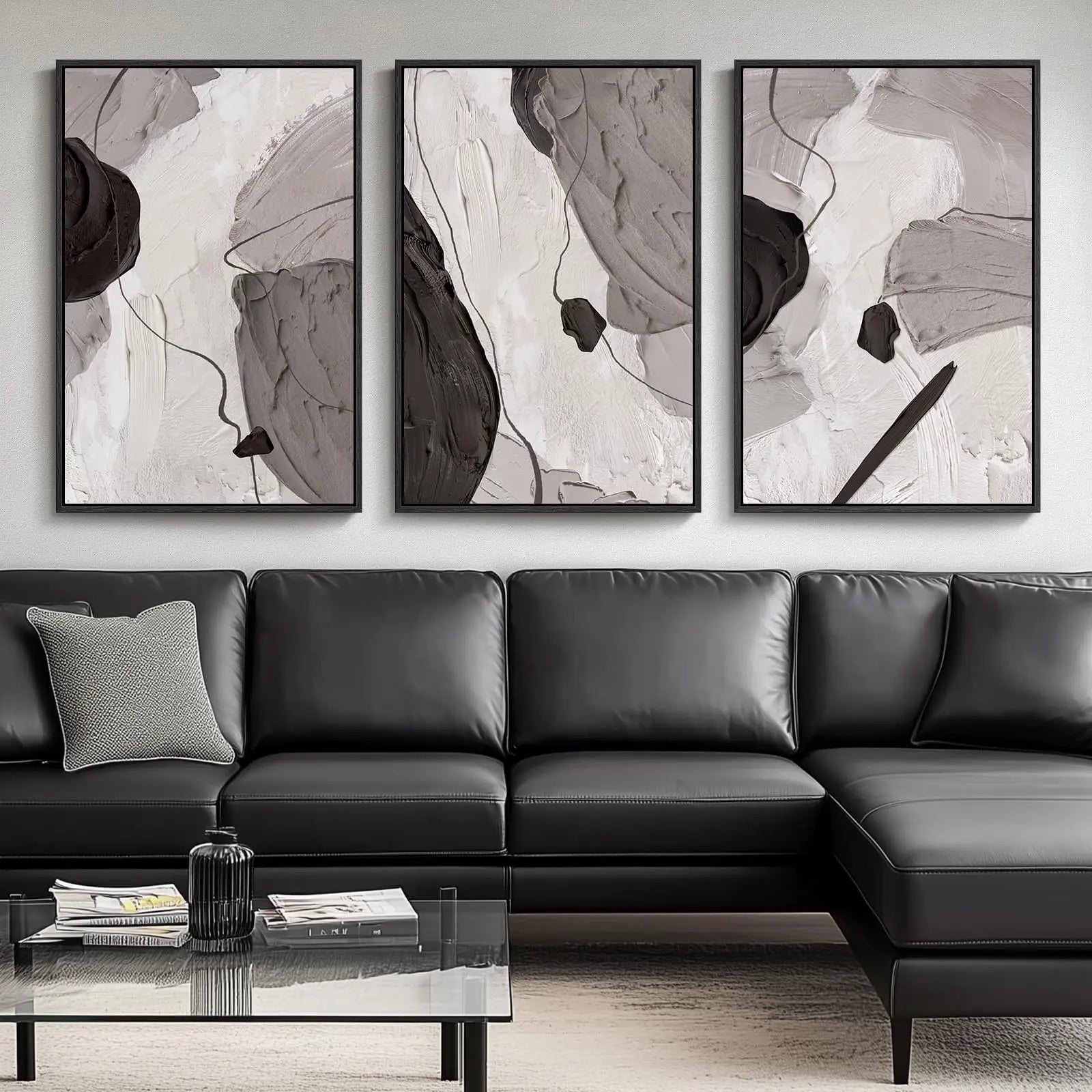 Three abstract art pieces above a black leather sectional sofa in a living room.