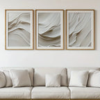Three abstract wall art pieces above a beige sofa with white cushions.