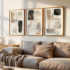 Three abstract paintings above a beige sofa with cushions in a living room setting.