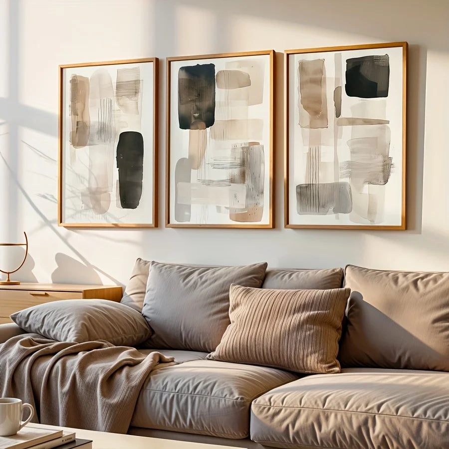Three abstract paintings above a beige sofa with cushions in a living room setting.