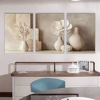Three framed artworks of floral and vase arrangements on a wall above a desk.