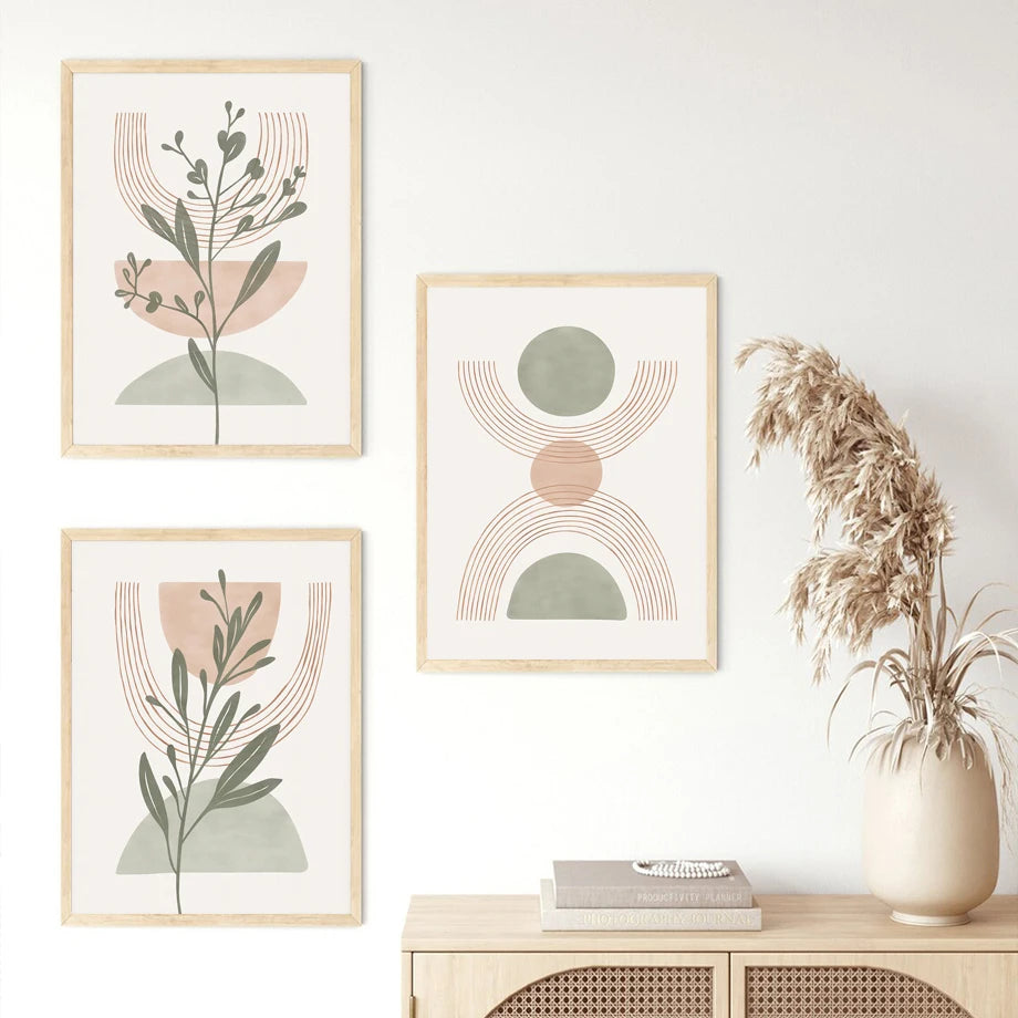 Three framed abstract art prints on a wall with a vase of dried plants on a table below.