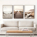 Three framed beach scenes above a beige sofa with a wooden coffee table.