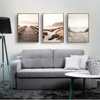 Gray sofa in a living room with three framed landscape pictures above it.