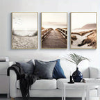 Three framed artworks of a beach scene above a white sofa with decorative pillows.