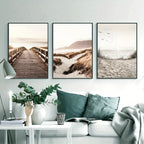 Three beach-themed wall art prints above a sofa with decorative pillows and a plant.