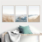Three framed beach-themed artworks above a bench with pillows.
