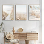Three framed artworks above a wooden console table in a room with a plant and chair.