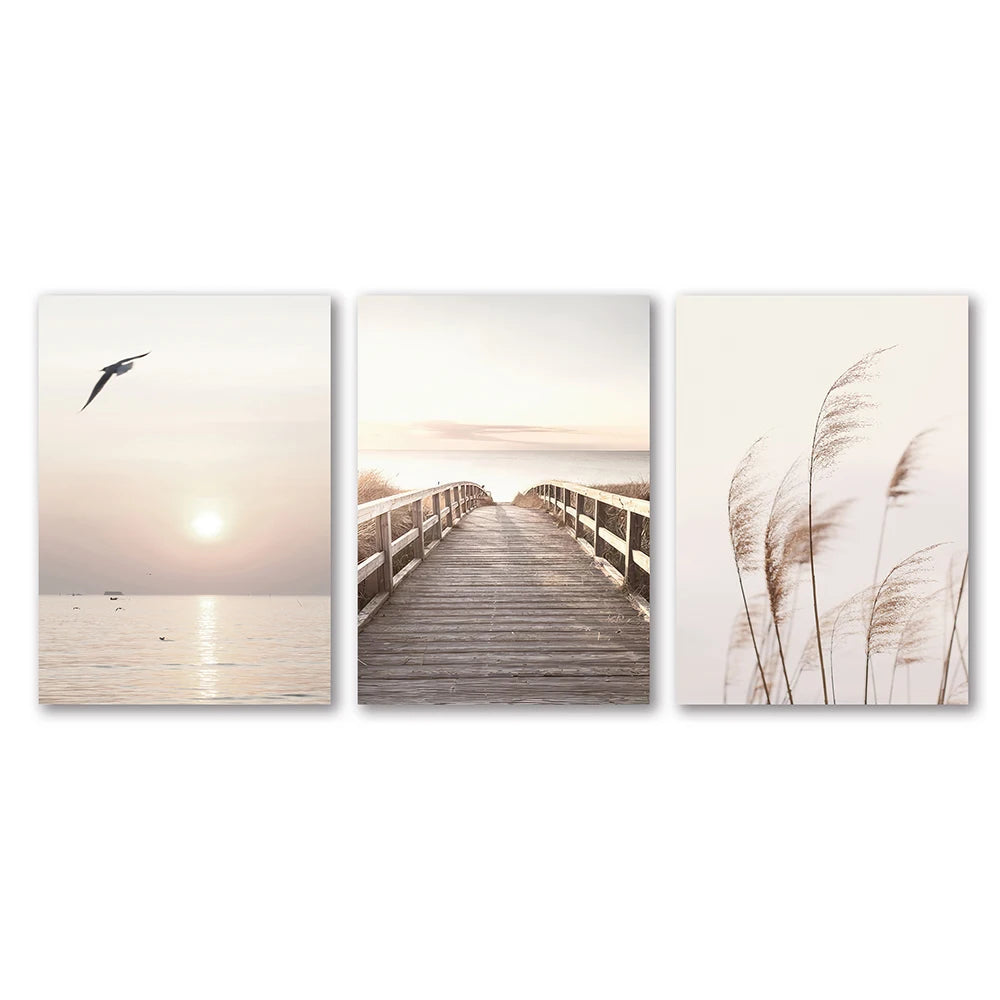 Set of three wall art prints featuring a beach scene with a sunset, a wooden boardwalk, and reeds.
