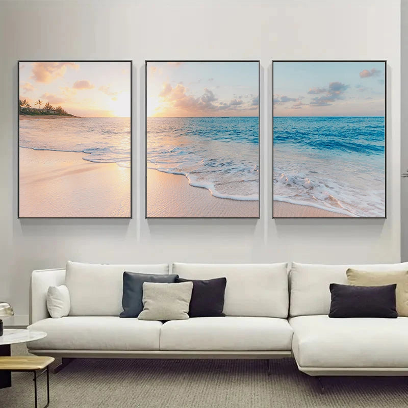 Three framed beach scenes above a white sofa with decorative pillows.
