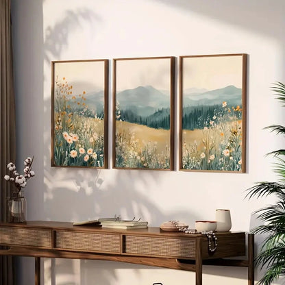 Three framed landscape paintings with mountains and flowers on a wall above a wooden console table.