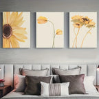 Three floral paintings above a bed with decorative pillows.