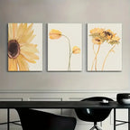 Three floral paintings on a wall above a black table with chairs.