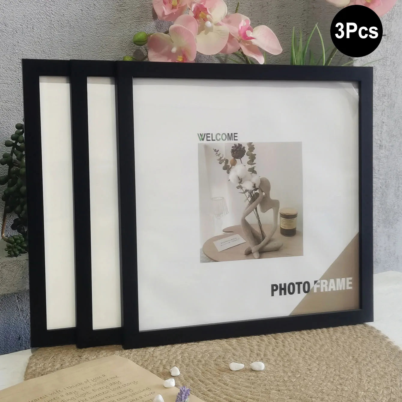 Set of three black photo frames with a decorative item inside, on a textured surface with flowers in the background.
