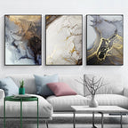 Three abstract art pieces on a wall above a white sofa with decorative pillows.