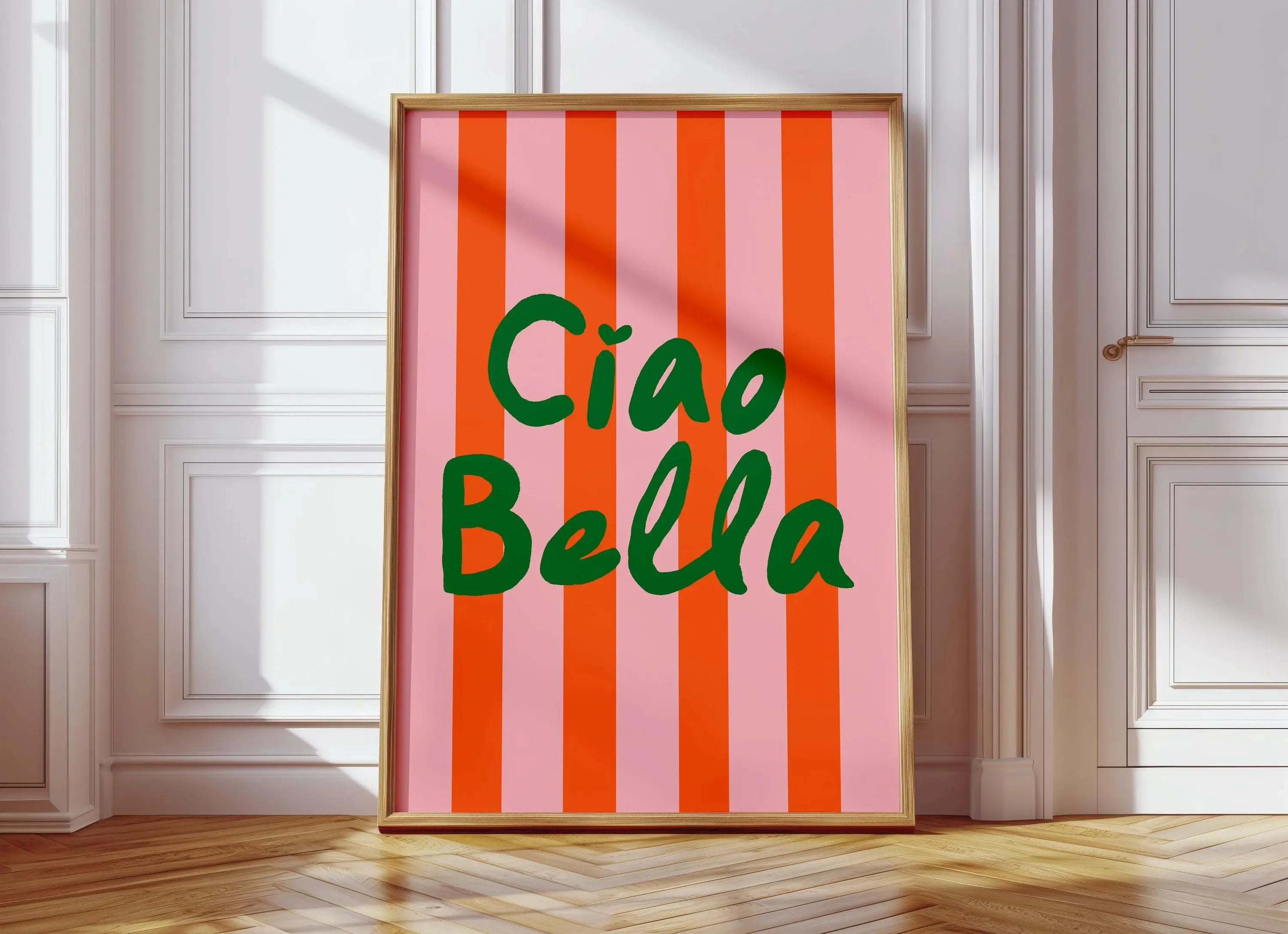 Framed artwork with 'Ciao Bella' text on a pink and orange striped background in a room.