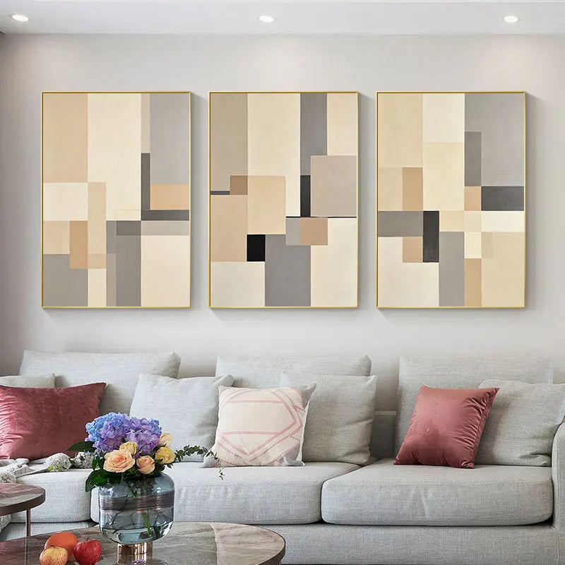 Three abstract art pieces on a wall above a sofa with decorative pillows.