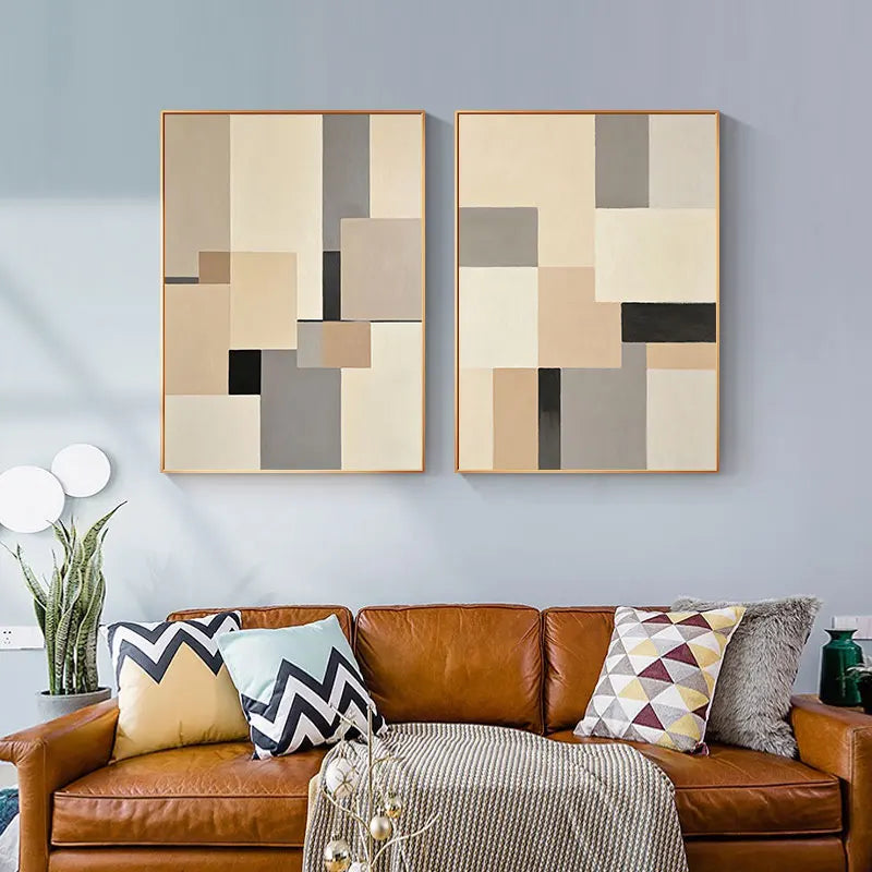 Two abstract wall art pieces above a brown leather sofa with decorative pillows.