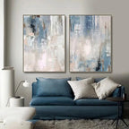 Two abstract art pieces on a wall above a blue sofa with decorative pillows.