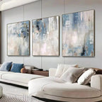 Three abstract paintings on a wall above a white sofa in a living room.