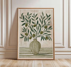 Framed artwork of a vase with green leaves and olives on a wall.