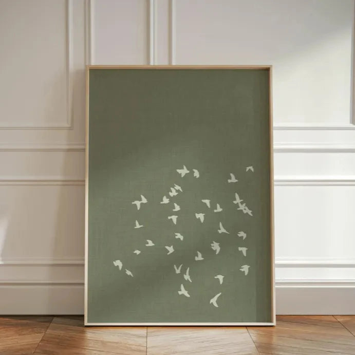 Framed artwork with white bird silhouettes on a green background against a neutral wall.