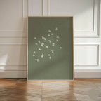 Framed artwork with white bird pattern on a green background, displayed in a room with wooden flooring and white paneled walls.