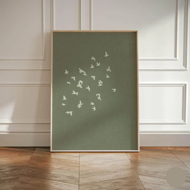 Framed artwork with white bird pattern on a green background, displayed in a room with wooden flooring and white paneled walls.
