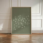 Framed artwork with white bird illustrations on a green background, displayed in a room with wooden flooring and white paneled walls.