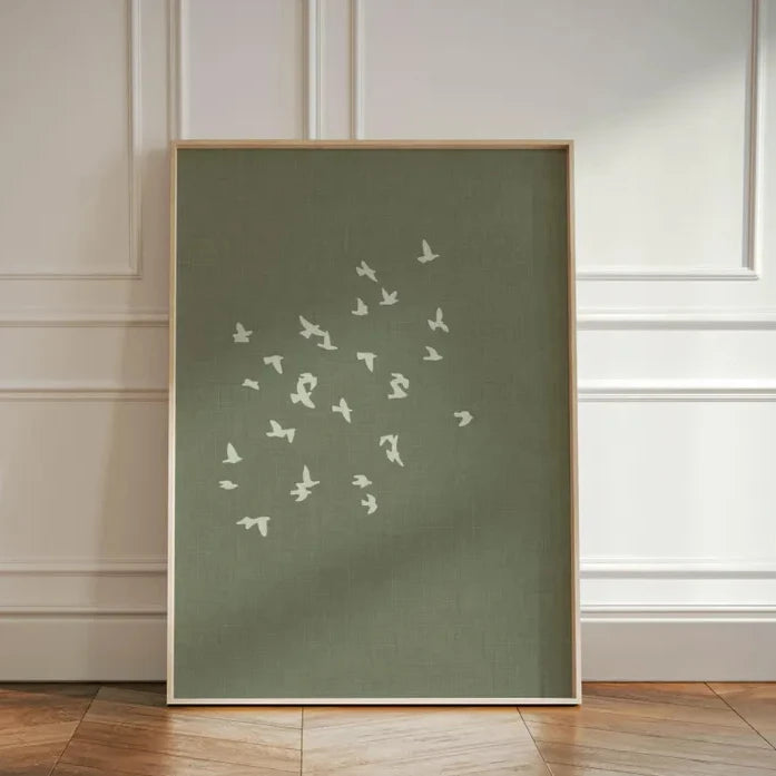Framed artwork with white bird illustrations on a green background against a white paneled wall.