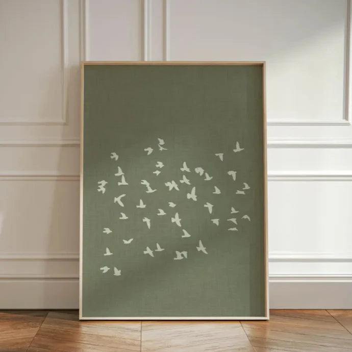 Framed artwork with white bird silhouettes on a green background against a white paneled wall.