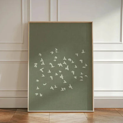Framed artwork with white bird silhouettes on a green background against a white paneled wall.