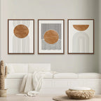 Three abstract art pieces in wooden frames on a wall above a white sofa.